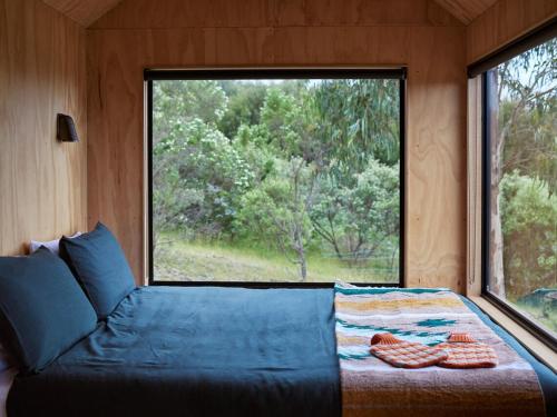 una cama en una habitación con una ventana grande en Ocean View Off-Grid Cabin Secluded in Nature - Govind, en Johanna