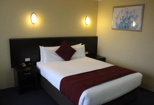 a hotel room with a bed with white sheets and red pillows at Alpine Motor Inn in Katoomba