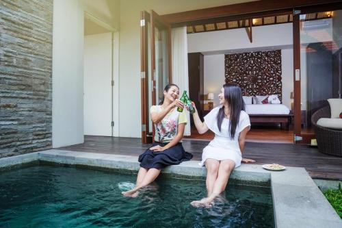 two women sitting on the edge of a swimming pool at Desa Di Bali Villas in Kerobokan