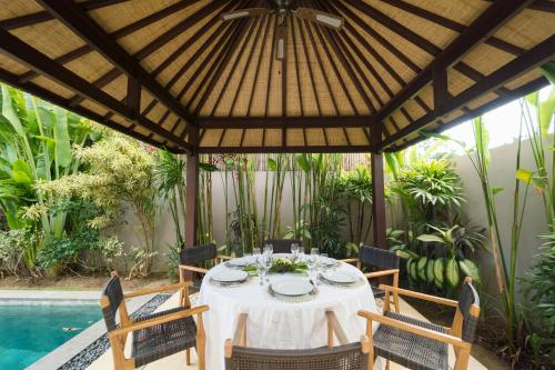 a dining table under a wooden pergola next to a pool at Desa Di Bali Villas in Kerobokan