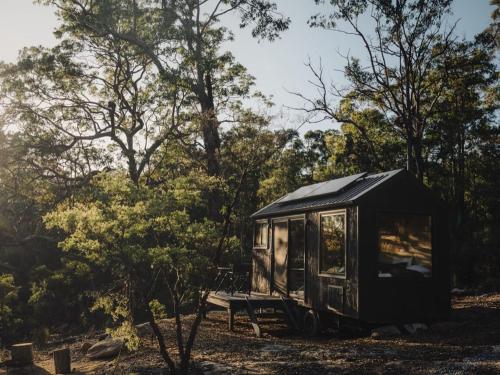 a black tiny house sitting in the woods at Off-Grid Cabin Nestled into Bush with Creek Access - Kaia in Kurrajong