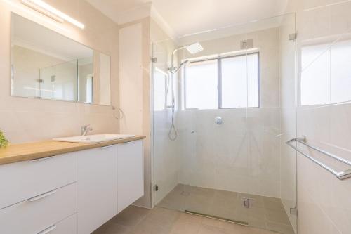 a white bathroom with a shower and a sink at Intrepid 12 right on the beachfront in Shoal Bay