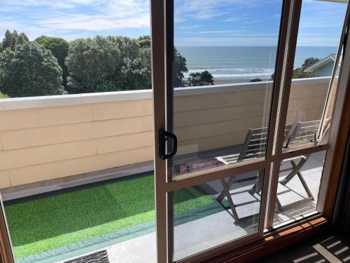 a view from a window with a chair on a balcony at 49 on Jans Beach Break in Oakura