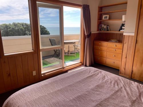 a bedroom with a large window with a view of the ocean at 49 on Jans Beach Break in Oakura