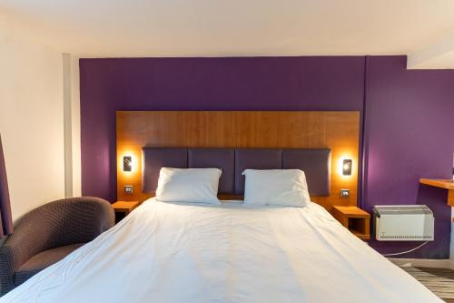 a bedroom with a large bed with a purple wall at Tyger Inn Derby in Derby