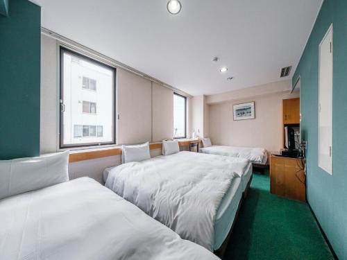 a hotel room with three beds and a window at Tabist THE GREEN OTARU in Otaru