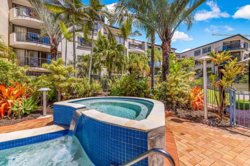 a swimming pool in front of a building with palm trees at Kalua Holiday Apartments in Maroochydore