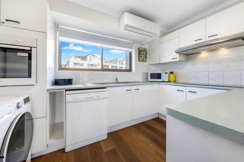 a white kitchen with white cabinets and a window at Kalua Holiday Apartments in Maroochydore