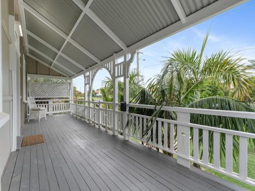 a porch with a white railing and palm trees at Silkstone Cottage in Bundamba