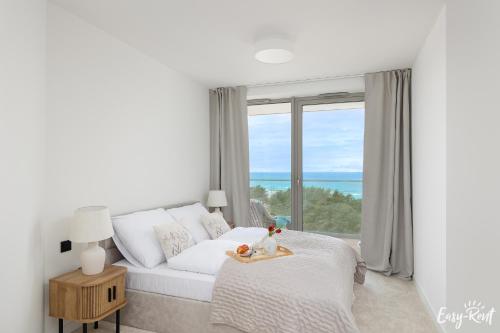 a white bedroom with a bed and a large window at Prestige Pinea 610 - basen, sauna, jacuzzi w cenie pobytu - Easy - Rent Apartments in Pobierowo