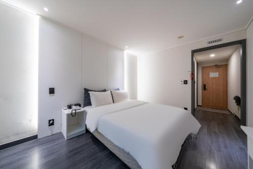 a white bedroom with a large white bed and a door at Hotel Kabo Pyeongtaek in Pyeongtaek
