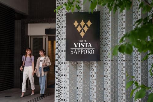 two women walking in front of a sign on a building at Hotel Vista Sapporo Odori in Sapporo