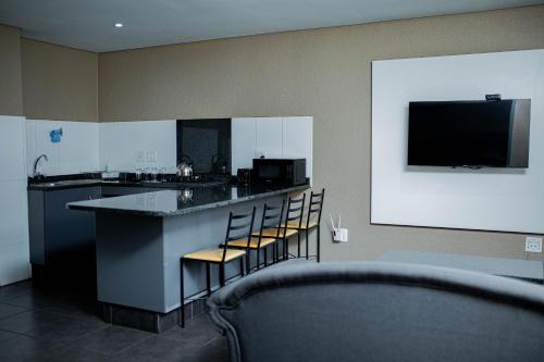 a kitchen with a bar with chairs and a tv at Vetho 2 Apartments OR Tambo Airport in Kempton Park