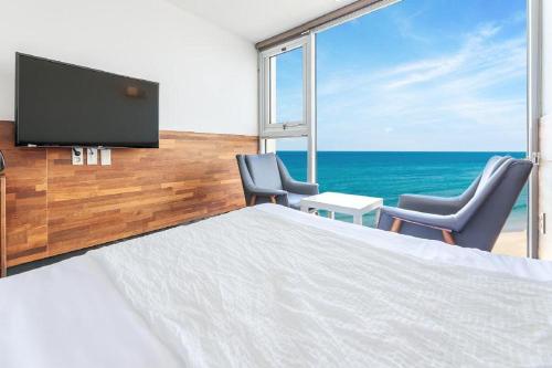 a bedroom with a bed and two chairs and a television at Jeju Dalbeach Pension in Jeju