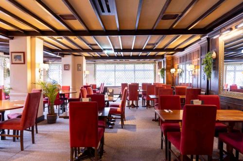 a dining room with tables and red chairs at Roebuck by Greene King Inns in Forest Row
