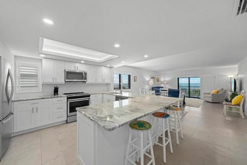 una cocina con armarios blancos y una gran isla con taburetes. en Sanddollar #A201, en Ybel