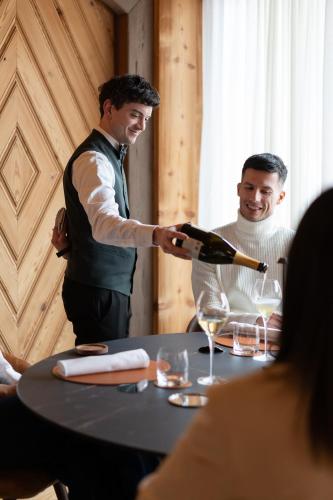 a man pouring a bottle of wine at a table at Hammerack Hotel, SPA & Wellness in Malborghetto Valbruna
