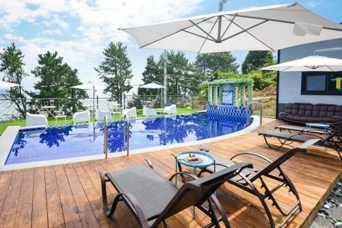 a deck with a pool with chairs and an umbrella at Yeosu Tivoli Pension in Yeosu