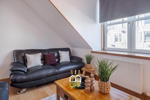a black leather couch in a living room with a table at Albyn Retreat - SJA Stays - 1 Bed Apartment in Aberdeen