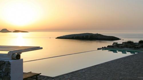 a swimming pool with a sunset in the water at Folegandros Villas Beachfront in Karavostasi