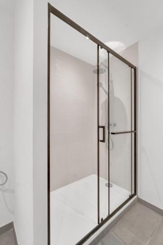 La salle de bains blanche est pourvue d'une porte de douche en verre. dans l'établissement Le quatre sansCuls - Proche gare, à Chambéry