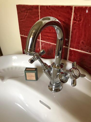 un robinet en argent sur un évier blanc avec une horloge dans l'établissement Tivauche, à Corsaint