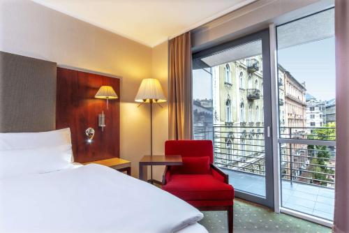 a bedroom with a bed and a red chair and a window at NH Budapest City in Budapest