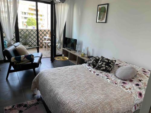 ein Schlafzimmer mit einem Bett und einem Stuhl und einem Fernseher in der Unterkunft Grand Studio avec Parking et Wifi in Castelnau-le-Lez