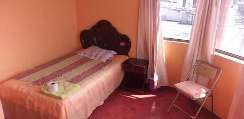 a bedroom with a bed and a chair and a window at Hostal Lesly Salomé in Tulcán