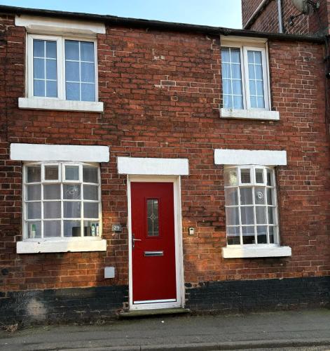 a brick building with a red door and two windows at West street home in Leek