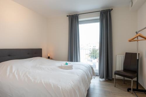 a bedroom with a white bed with a chair and a window at Wonderful new apartment close to the beach in Ostend