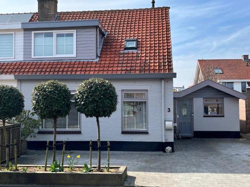 a white house with a red roof and two trees at Appartement Scheepswerf in Burgh Haamstede