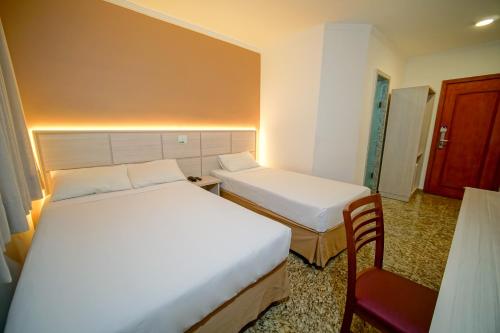 a hotel room with two beds and a chair at Hotel Golden Park Sorocaba & Convenções by Nacional Inn in Sorocaba