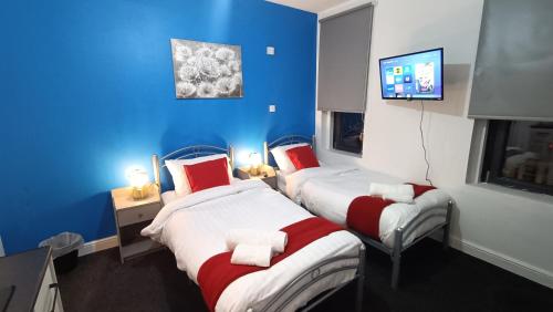 two beds in a room with blue walls and a tv at Comforatable Modern Studios in Nottingham