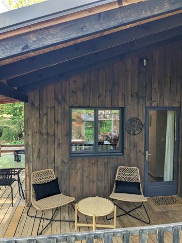 une terrasse en bois avec des chaises, une table et une fenêtre dans l'établissement Lodge Hérisson avec Spa privatif, à Biron
