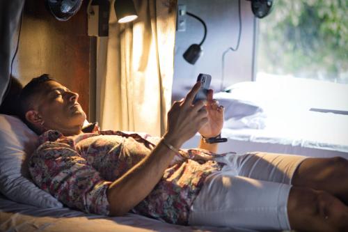 a man laying on a bed taking a picture with his cell phone at Ceiba Hostel in Fortuna