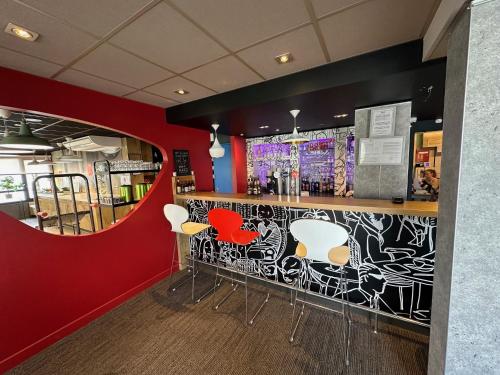 a bar with white chairs and a red wall at ibis Cambrai in Cambrai