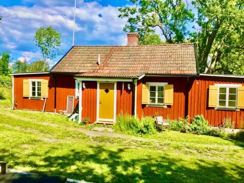 a red house with a yellow door in a yard at Fairy Lake Retreat! Uniquely Located House with Dock! in Bålsta