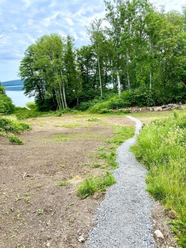 a dirt road with trees and water in the background at Fairy Lake Retreat! Uniquely Located House with Dock! in Bålsta