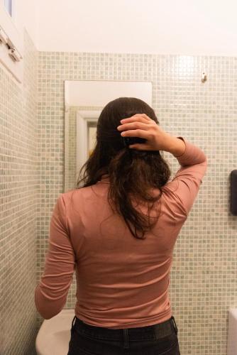 a woman standing in front of a bathroom mirror at Sunflower Beach Backpacker Hostel & Bar in Rimini
