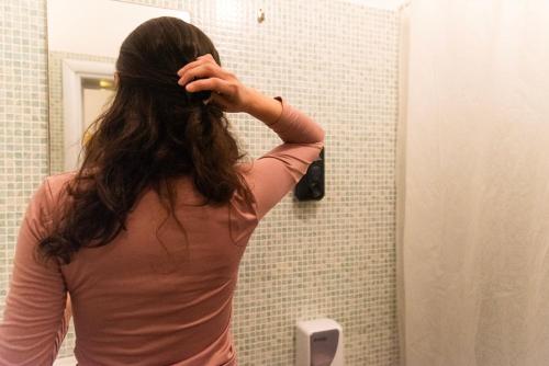 a woman brushing her hair in a bathroom mirror at Sunflower Beach Backpacker Hostel & Bar in Rimini