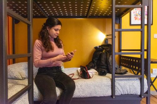 a woman sitting on a bed looking at her cell phone at Sunflower Beach Backpacker Hostel & Bar in Rimini