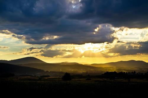 a sunset with the sun shining through the clouds over mountains at Apartament Słoneczny in Wałbrzych