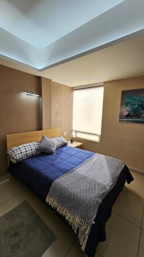 a bedroom with a bed with a blue comforter and a window at PLAZA ACEQUIA SUITES para 1 a 4 personas ESPECIALISTAS CORTAS MEDIANAS Y LARGAS ESTANCIAS en IZCALLI TEPOTZOTLAN perfectas para Familias, Turistas, Contratistas, Estudiantes, Empresas y Ejecutivos 5 min Izcalli 15 min Esmeralda 20 min Satélite 25 min AIFA in Cuautitlán Izcalli