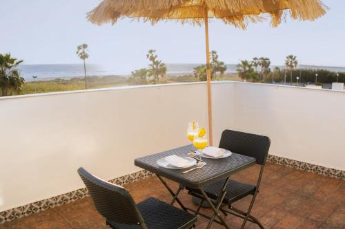 stół z 2 krzesłami i parasol na balkonie w obiekcie Hotel Playa Conil - Beachfront Studios & Suites w mieście Conil de la Frontera