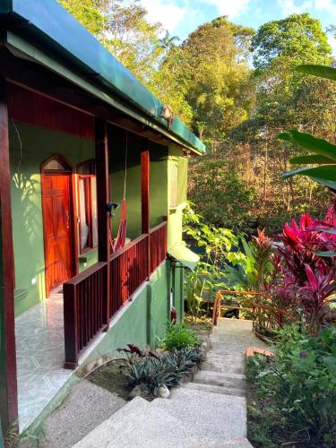 a green house with a red door and some plants at Corcovado & Drake Inn in Drake