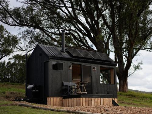 a black tiny house sitting on top of a field at Off-Grid Cabin with Valley Views and Hot Tub - Pepe in Tarra Valley