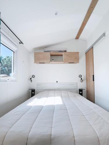 un grand lit blanc dans une chambre avec une fenêtre dans l'établissement Le Ti Buch Mobilhome en Camping 4 étoiles avec Terrasse Plancha et Climatisation, à La Teste-de-Buch
