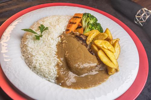 a plate of food with rice and meat and vegetables at Le Piège Motel Thematiquè in Almirante Tamandaré