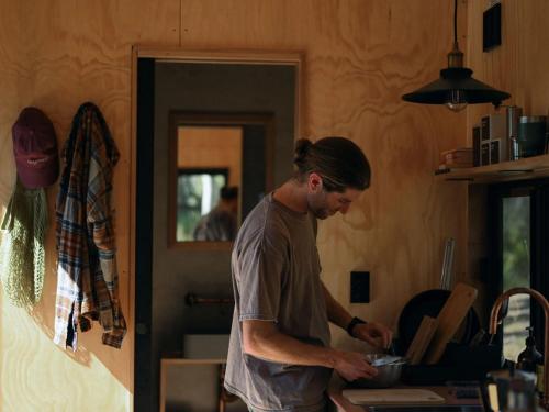 a man standing in a kitchen preparing food in a bowl at Off-Grid Cabin with Valley Views and Hot Tub - Velma in Tarra Valley